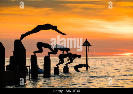 Aberystwyth Wales Uk, Thursday 17 May 2018  UK Weather:  At sunset at the end of a glorious day of warm spring sunshine, a group of university students are silhouetted as they dive  and jump into the clear water off the wooden pier at Aberystwyth on the west coast of Wales  photo © Keith Morris / Alamy Live News Stock Photo