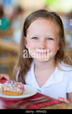 Adorable little girl enjoying eating donut at cafe Stock Photo