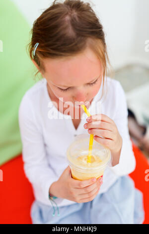 Adorable little girl drinking fresh smoothies on a colorful pillows at outdoor cafe on summer day Stock Photo
