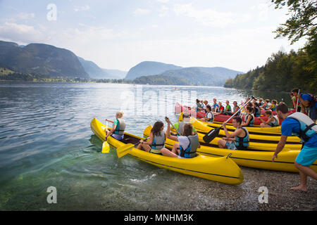 Young adults of school class are entering water of lake Bohinj with canoes, largest permanent lake located in Bohinj Valley of Julian Alps, Triglav National Park, Slovenia Stock Photo