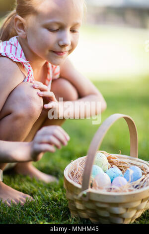 Adorable little girl holding a basket with Easter eggs outdoors on spring day Stock Photo