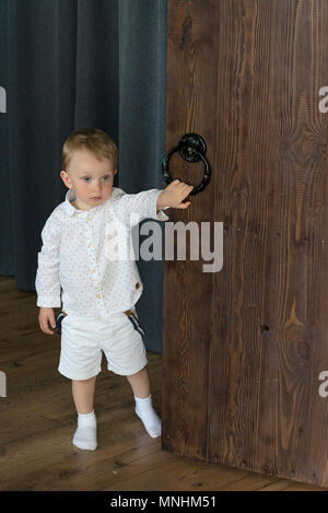 A little boy near the wooden door. Opens or closes the door. Stock Photo