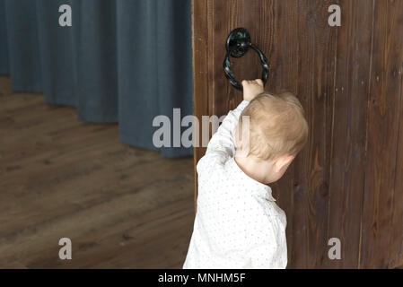 A little boy near the wooden door. Opens or closes the door. Stock Photo