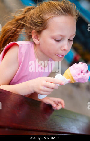 Adorable little girl eating ice cream in a fresh waffle cone in outdoor cafe on summer day Stock Photo