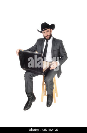 A handsome young business man sitting with his briefcase on his knees wearing a black cowboy hat, isolated for white background Stock Photo