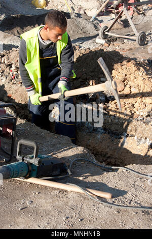 Belgrade, Serbia - November 5, 2017 : Young worker on road construction site digging with pickaxe , and a drilling machine laying next to him Stock Photo