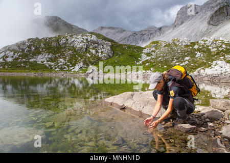 Ranger of Triglav National Park collecting drinking water from lake near Krn mountain, Julian Alps, Slovenia Stock Photo