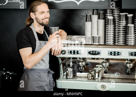 Portrait of a handsome barista in uniform standing near the coffee machine in the coffee shop Stock Photo