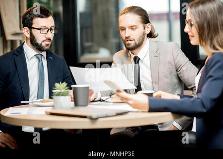 Three business people working with documents sitting together during the coffee break in the modern cafe interior Stock Photo