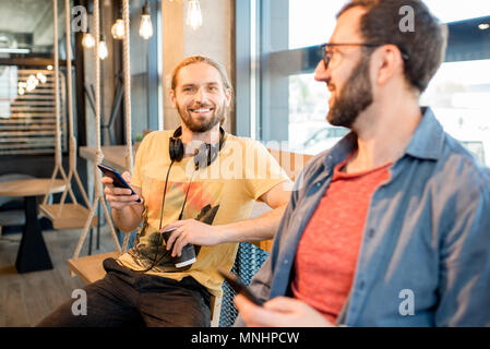 Two friends having fun sitting together with phones in the cafe Stock Photo
