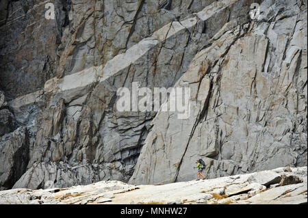 Backpacker hikes under a granite wall in Palisade Basin on a two-week trek of the Sierra High Route in Kings Canyon National Park in California. The 200-mile route roughly parallels the popular John Muir Trail through the Sierra Nevada Range of California from Kings Canyon National Park to Yosemite National Park. Stock Photo