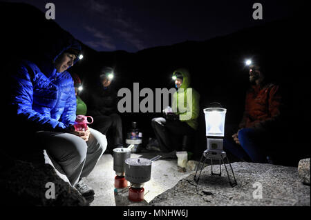 Backpackers have dinner with headlamps sitting at camp on the Barrett Lakes in Palisade Basin on a two-week trek of the Sierra High Route in Kings Canyon National Park in California. The 200-mile route roughly parallels the popular John Muir Trail through the Sierra Nevada Range of California from Kings Canyon National Park to Yosemite National Park. Stock Photo