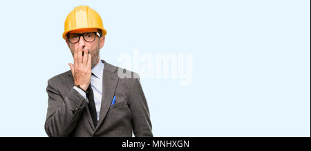 Senior architect or engineer covers mouth in shock, looks shy, expressing silence and mistake concepts, scared isolated over blue background Stock Photo