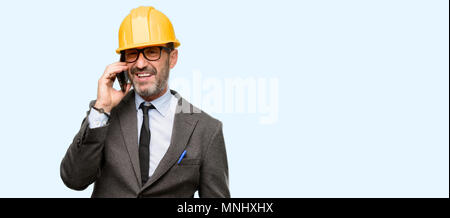 Senior architect or engineer happy talking using a smartphone mobile phone isolated over blue background Stock Photo