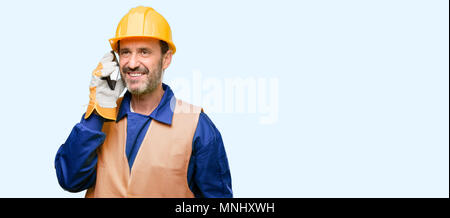 Senior engineer man, construction worker happy talking using a smartphone mobile phone isolated over blue background Stock Photo