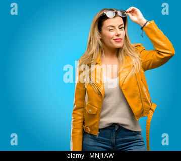 Beautiful young woman blinking eyes with happy gesture, blue background Stock Photo