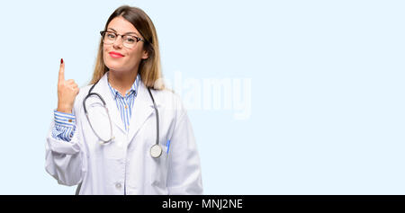 Young doctor woman, medical professional raising finger, the number one Stock Photo