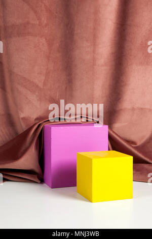 Two bright yellow and pink cubes in front of an old pink velvet curtain. Minimal color still life photography. Stock Photo
