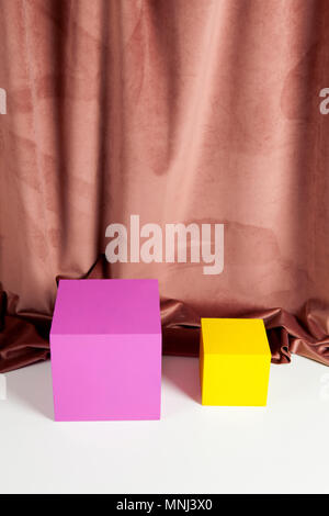 Two bright yellow and pink cubes in front of an old pink velvet curtain. Minimal color still life photography. Stock Photo