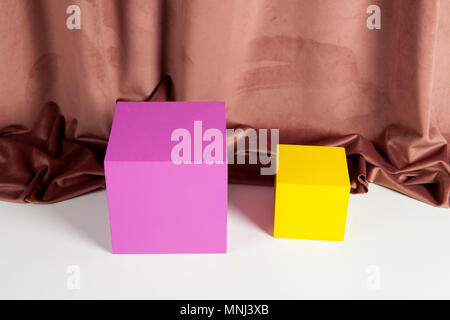 Two bright yellow and pink cubes in front of an old pink velvet curtain. Minimal color still life photography. Stock Photo