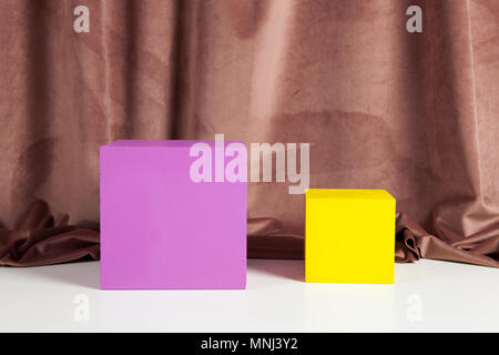 Two bright yellow and pink cubes in front of an old pink velvet curtain. Minimal color still life photography. Stock Photo