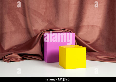 Two bright yellow and pink cubes in front of an old pink velvet curtain. Minimal color still life photography. Stock Photo
