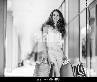 A brown-haired woman wearing muted, gentle shades holds five colourful, patterned shopping bags during a successful shopping spree. Walking outside, s Stock Photo