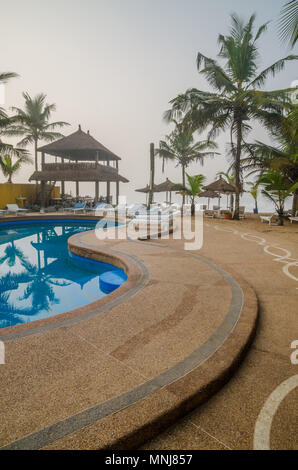 Holiday resort with pool, palm trees and thatched shelters at coast Stock Photo