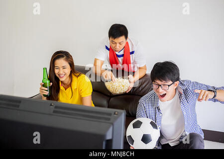 People watch soccer. Asian football supporters watching soccer on television at home with happy emotion. Stock Photo