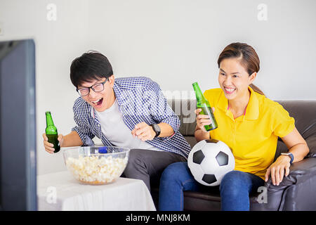 People watch soccer. Asian football supporters watching soccer on television at home with happy emotion. Stock Photo