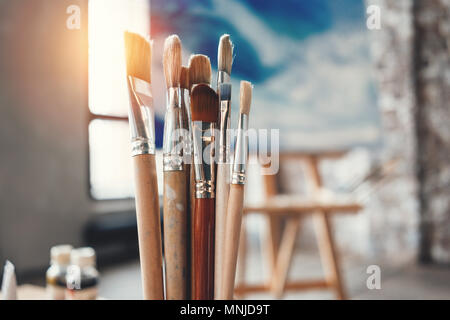 Artist paintbrushes closeup on blurred background of painter workshop. Different brushes in drawing studio interior. Flare effect Stock Photo