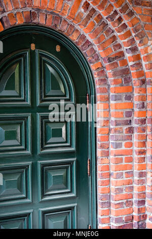 Old strong painted arched wood entrance door with convex panels arranged in two rows framed by brick arch of the building as a symbol of a reliable pa Stock Photo