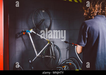 Services professional washing of a bicycle in the workshop. Close-up of hand Young Caucasian stylish man doing bicycle cleaning using automatic electric water pump. Sprays scatter from the pressure Stock Photo