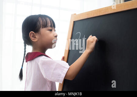 Asian Chinese little girl writing on blackboard in isolated white background Stock Photo