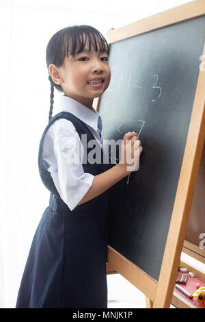 Asian Chinese little girl writing on blackboard in isolated white background Stock Photo
