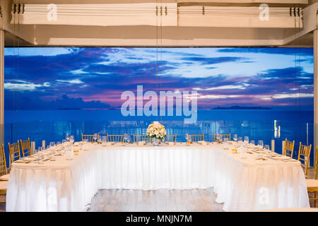 The blue sky with ocean view at the wedding reception dinner table setting with white tablecloth in U shape for dinner, bouquet decoration at the brid Stock Photo