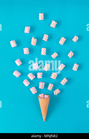 Waffle cone with marshmallow bouquet on blue surface. Flat lay, top view sweet food background. Stock Photo