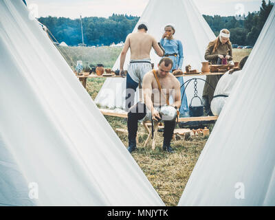 RITTER WEG, MOROZOVO, APRIL 2017: Outdoor scene of medieval way of life. The guy cleans the helmet after an improvised battle of knights. In the background, a field kitchen and a medieval camp. Stock Photo