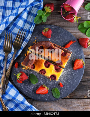 two pieces of cheesecake with strawberries on a black graphite plate, top view, next to fresh ripe berries Stock Photo