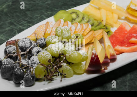 Sliced fruit on a white plate, grapes, kiwi, orange, pear Stock Photo
