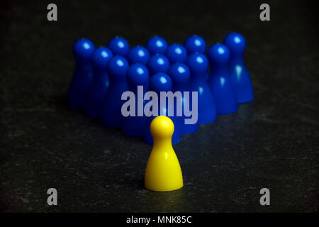 one yellow pawn and a group of blue pawns on a table Stock Photo