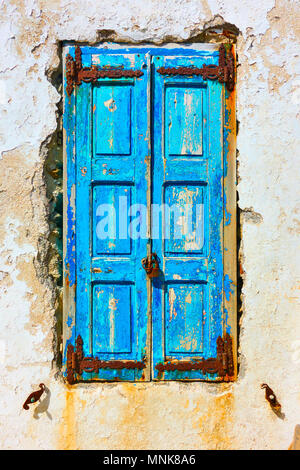Old window with closed shabby blue shutters, Mykonos, Greece Stock Photo