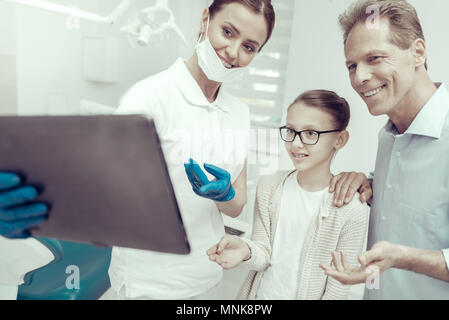 Smiling dentist looking at the screen of a tablet together with her patients Stock Photo