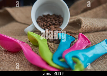 Loose roasted coffee beans, white porcelain coffee mug and color plastic dose measuring spoons on jute sack. Conceptual of recommended amount of coffe Stock Photo