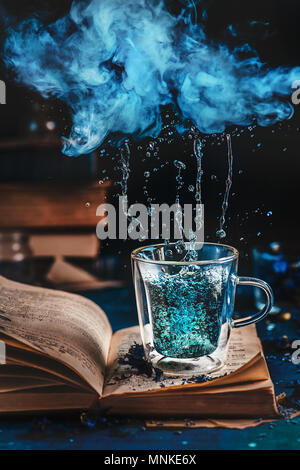 Double wall glass cup of blue tea on an open book under a raining cloud of vapor. Rainy weather reading concept Stock Photo