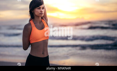 Woman runner stretching hands at the beach. Female athlete warming up before a run in morning at the beach. Stock Photo
