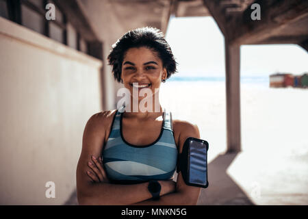 Portrait of fitness woman standing outdoors and smiling. Female athlete taking a break after training session. Stock Photo