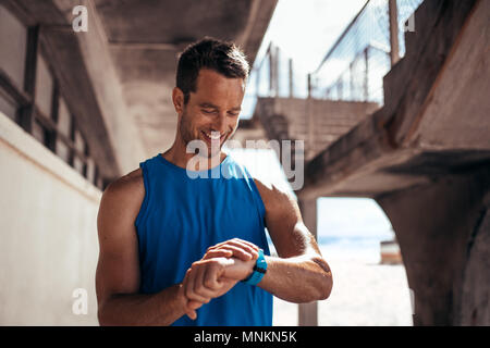 Smiling man using a smartwatch to monitor his progress. Male athlete checking his performance on fitness app on his smartwatch.. Stock Photo