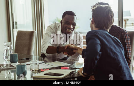 Businessmen discussing work sitting at conference table in office. Men shaking hands and smiling during a business meeting. Stock Photo