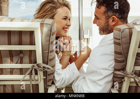 Loving couple in looking at each other and smiling outdoors. Smiling man and woman sitting on deck chairs with a glass of wine. Stock Photo